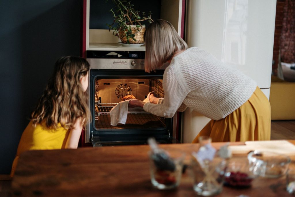 Mother taking cake from oven while daughter observes