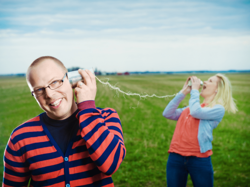 Man and woman on lawn communicating through a tin can telephone